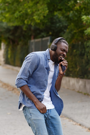 Young Afro-American man in headphones listening music on smart phone using music app. Portrait of...