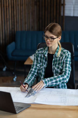 Architect drawing blueprints in office. Engineer sketching a construction project. Architectural plan. Close-up portrait of beautiful woman concentrated on work. Business construction concept.の写真素材