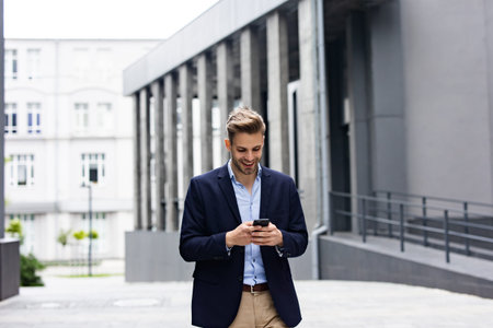 Handsome businessman using smartphone and smiling. Happy young man using mobile phone apps, texting...
