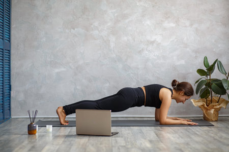 Young sporty female yoga instructor coaching online, making video of yoga lessons on laptop camera....