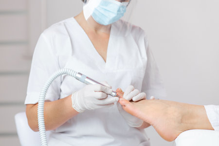 Peeling feet with special electric device.Professional hardware pedicure using electric machine.Patient on medical pedicure procedure, visiting podiatrist.Foot treatment in SPA salon.Podiatry clinicの写真素材