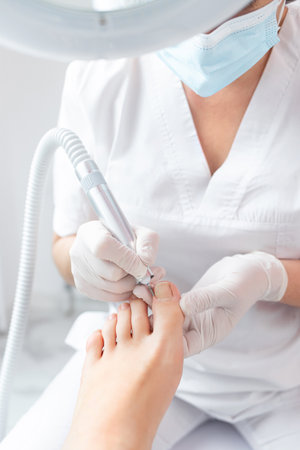 Peeling feet with special electric device.Professional hardware pedicure using electric machine.Patient on medical pedicure procedure, visiting podiatrist.Foot treatment in SPA salon.Podiatry clinicの写真素材
