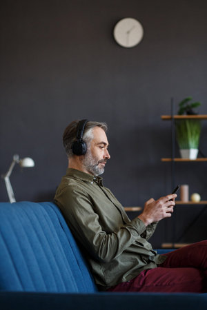 Senior man in headphones listening music on smart phone using music app. Portrait of handsome...