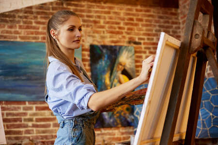 Young beautiful female artist painting on canvas using oil paintings and art brush. Painter creating artwork in art studio. Relaxation, leisure, hobby, stress managementの写真素材