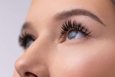 Close up portrait of woman face. Young, beautiful girl with fresh soft skin combing long black eyelashes with special mascara brush. Fake eyelashes. Eyelashes extensions close upの写真素材