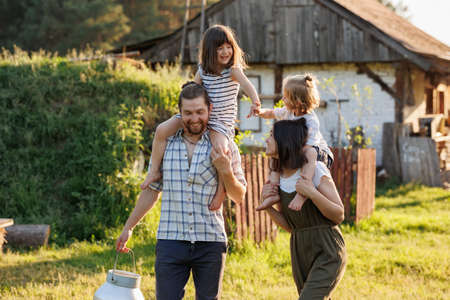 Happy young family enjoy spending time together on weekend at the countryside. Mother, father and two kids walking near their wooden country house. Moving from urban areas to rural areas concept.の写真素材