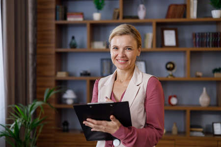 Portrait of beautiful smiling female psychologist taking notes on clipboard. Professional psychotherapist working in modern office.の写真素材