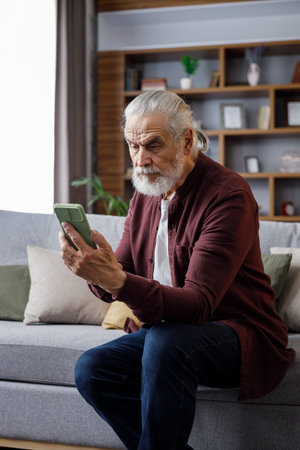 Smiling elderly gray-haired man using smartphone for texting message, playing video games, watching...