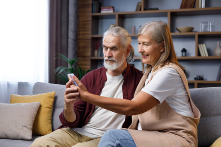 Mature happy couple communicates online call. A gray-haired husband and wife are talking to relatives on the phone. Video call on smartphone. Remote communicationの写真素材