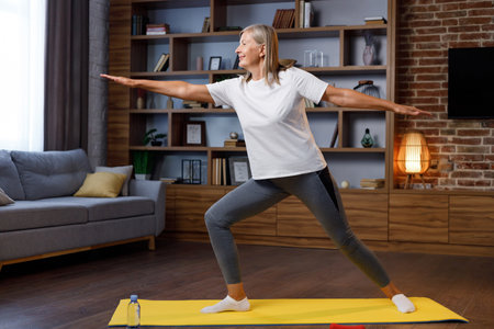 Gray-haired happy mature woman doing gymnastics and yoga at home online with laptop. Active and healthy lifestyle for pensioners. Fitness lessons online, recreation, well-being of the elderly.の写真素材