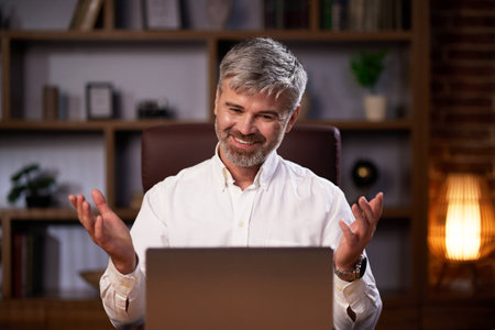 Portrait of a businessman in the office smiling and looking at the camera. Successful european man in white shirt sitting at work desk and having online video call while working remotelyの写真素材