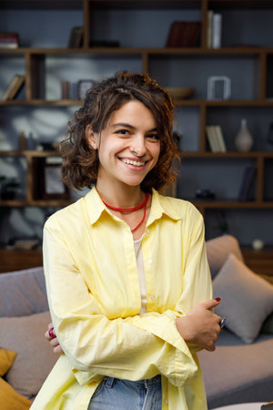 A beautiful, curly-haired girl looks into the camera and smiles, a dazzling smile. Video portrait of a woman in a home office. Posing for a close-up portrait.の写真素材