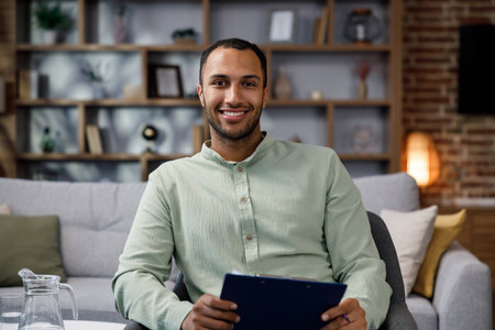 Young African American man sitting at home in a stylish office. Psychologist, coach or businessman looking at the camera and smiling. Beautiful teeth and smile.の写真素材