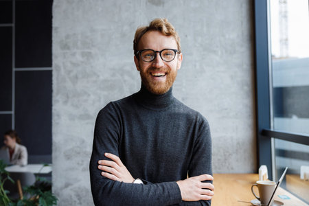 A young red-haired guy, a programmer or an entrepreneur in glasses, in a stylish cafe Looks at the...