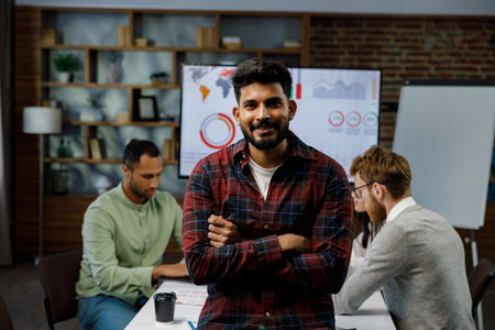 Confident smiling Indian guy, startup team leader, standing in front of mixed race office workers or business people with arms crossed or clasped, looking at the camera. business conceptの写真素材