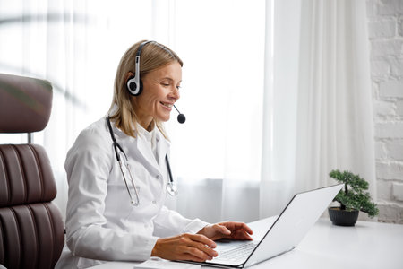 Telemedicine. Headshot portrait of smiling female doctor in headphones looking at camera. A female medical doctor remotely consults in a virtual online meeting with a patient. Online medicineの写真素材