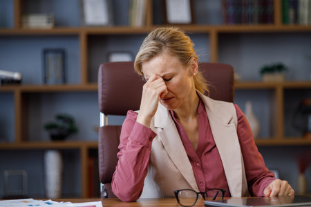 Tired businesswoman after exhausting paperwork taking off eyeglasses feeling nack pain. Head ache, bad vision, chronic fatigue and eyestrain concept. Burnout and overwork conceptの写真素材