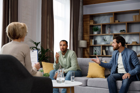 Family quarrel at the reception at the psychologist. LGBT couple at a psychotherapists appointment. Psychologist for gays. Support for the LGBT community in visiting a psychologist.の写真素材