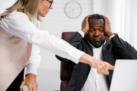 Angry female boss scolding African American office worker. A demanding manager-leader is annoyed by laziness and mistakes in the work of an employee. Authoritarian leadership, malfeasance, racismの写真素材