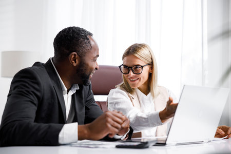 Two people analyze documents on a laptop while sitting at a table in the office. Business partners at work in the office are discussing projects. Multi-racial collaboration.の写真素材