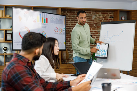 Motivated african american businessman having business meeting with managers, negotiating, using presentation tv with statistics, charts, big data. Digital entrepreneurs work on an e-commerce project.の写真素材