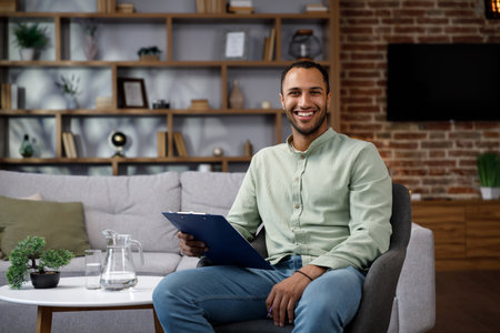 Young African American man sitting at home in a stylish office. Psychologist, coach or businessman looking at the camera and smiling. Beautiful teeth and smile.の写真素材