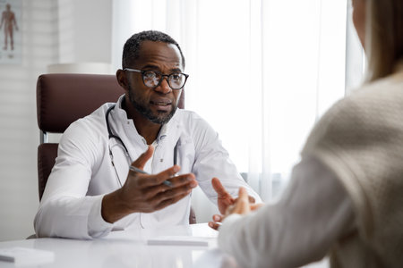 African American doctor, receives a patient, listens to complaints, makes diagnostics. Writes data. Doctors appointment.の写真素材
