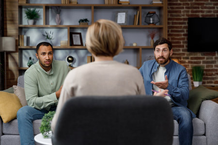 Family quarrel at the reception at the psychologist. LGBT couple at a psychotherapists appointment. Psychologist for gays. Support for the LGBT community in visiting a psychologist.の写真素材