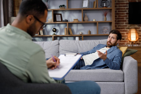 Visit to a psychologist. A handsome man is lying on the couch and talking to a psychotherapist. The patient is in depression, apathy and stress from burnout at work. Help of a psychologist.の写真素材