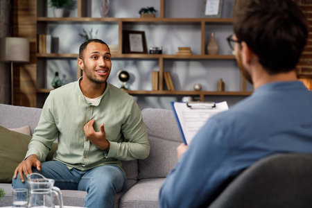 Visiting a psychologist A man sits on a couch and talks to a psychotherapist. He thanks the doctor and smiles, therapy helped him. Help of a psychologist.の写真素材