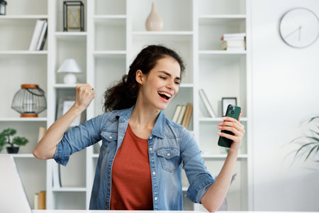 Happy young girl looks at the phone and rejoices at the good news, wins the lottery. Enjoyed woman screams at the screen of the phone.の写真素材