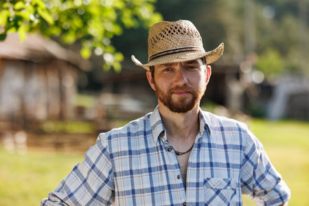 Portrait of young Caucasian handsome bearded male farmer smiling to camera. Happy rancherman in straw hat at the eco farm. Industrial production of goat milk dairy products. Cattle farmingの写真素材