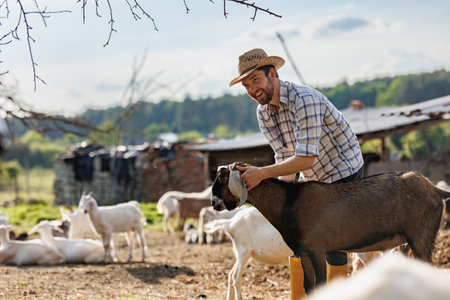 Male farmer taking care of his cute goats. Young rancherman getting pet therapy. Animal husbandry for the industrial production of goat milk dairy products. Agriculture business and cattle farming.の写真素材