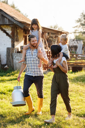 Happy young family enjoy spending time together on weekend at the countryside. Mother, father and two kids walking near their wooden country house. Moving from urban areas to rural areas concept.の写真素材