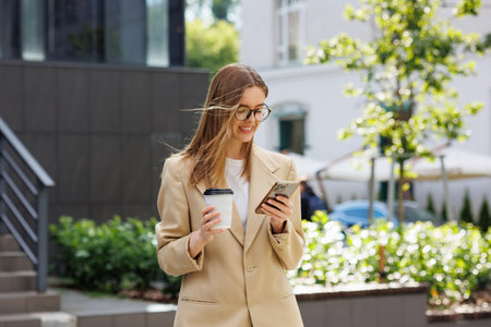 A young blonde girl against the backdrop of a business center, office center. Portrait of a successful startup. Smartphone, coffee casual suit.の写真素材