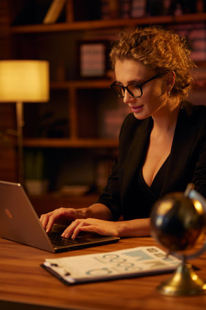 Purposeful young business woman, professional entrepreneur, works behind a laptop. Businesswoman, in a beautiful office in cinematic light. Finance, startups, stock trading, online workの写真素材
