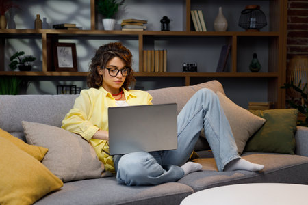Serious young female freelancer working freelance from home. Works sitting on sofa on laptop, focused girl using computer to study online at home, female user, internet remote work, programmingの写真素材