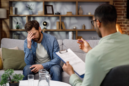 Visit to a psychologist. A man sits on a couch and talks to a psychotherapist. The patient is depressed, apathetic and stressed from problems in his personal life. Help of a psychologist.の写真素材