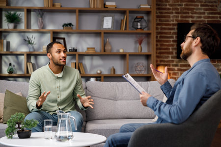 Visiting a psychologist A man sits on a couch and talks to a psychotherapist. He thanks the doctor and smiles, therapy helped him. Help of a psychologist.の写真素材
