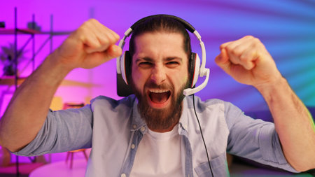 Gamer bearded guy, in a gaming headset, wins a video game. Cybersportsman in a neon room. Lifestyle gamer, online games. Victory in the E-Sport tournamentの写真素材