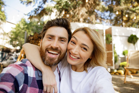 A lovely couple are sitting near the travel trailer, taking a selfie, laughing having fun, enjoying their vacation. Portrait of in love enjoying a sunny day outside the city, camera view.の写真素材
