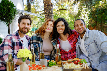 A group of friends are relaxing in nature. Two girls and two boys of different races are looking at the camera, smiling, having fun on the background of a travel trailer.の写真素材
