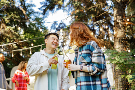 Two friends are relaxing near a travel trailer. A couple of a red-haired girl and an Asian guy are drinking drinks in the company of friends.の写真素材