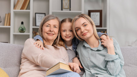 Little granddaughter hugs 60-year-old grandmother and young mother, showing love on Mothers Day, looking at the camera. A portrait of family love, the connection of generations.の写真素材