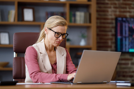 Portrait of adult businesswoman working with laptop at office. Female trader texting messages, doing paperwork with stock market graphs on background. The rise and fall of cryptocurrencies conceptの写真素材
