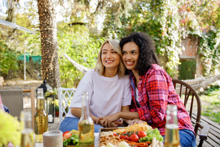 Two friends are having fun at a picnic table. A blonde european and afroamerican girls are hugging on a picnic in the forest outside the city.の写真素材