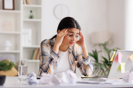 A tired young Indian girl gets angry from the number of tasks, crumples up the paper and throws it away, tries to calm down by meditating. Stressful work and study, overtasking, headache.の写真素材