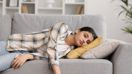 Tired Indian girl slumps on couch feeling listless. Feeling depressed, lack of motivation, sadness, boredom. Exhausted, he collapses on the couch from stress. Burn out.の写真素材