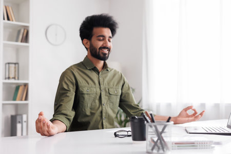 Managing stress in the workplace. Business man meditating and relaxing during a busy day while sitting at workplace in office interior. The concept of mental health.