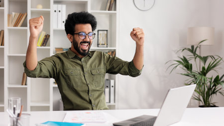 Satisfied Indian man in black glasses checking his email and happy with good news. A young man winner celebrating the victory, raises his hands uphill.の写真素材